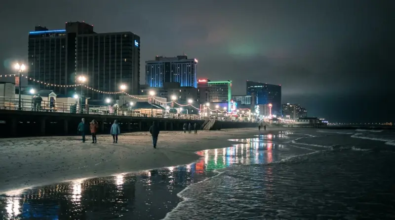 The Atlantic City boardwalk and casino towers lit at night, seen from the beach