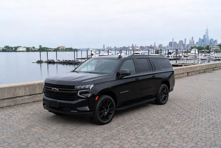 A black Chevrolet Suburban on the waterfront with the Manhattan skyline behind it